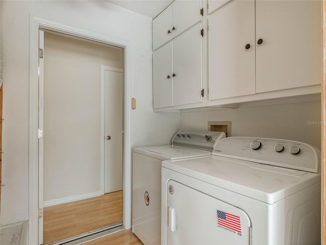 laundry room with a textured ceiling, washing machine and dryer, light hardwood / wood-style floors, and cabinets