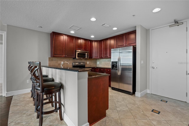 kitchen featuring light tile patterned floors, backsplash, a textured ceiling, a kitchen bar, and stainless steel appliances