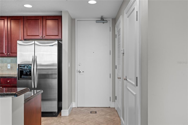 kitchen with decorative backsplash, light tile patterned flooring, stainless steel refrigerator with ice dispenser, and dark stone countertops