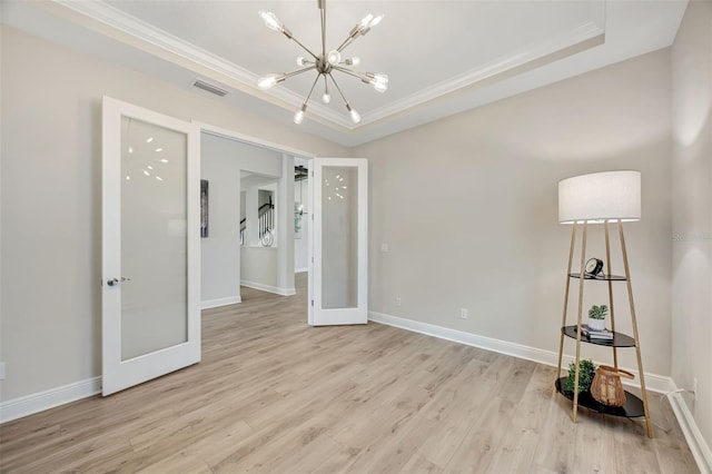 spare room featuring french doors, a raised ceiling, crown molding, a notable chandelier, and light hardwood / wood-style floors