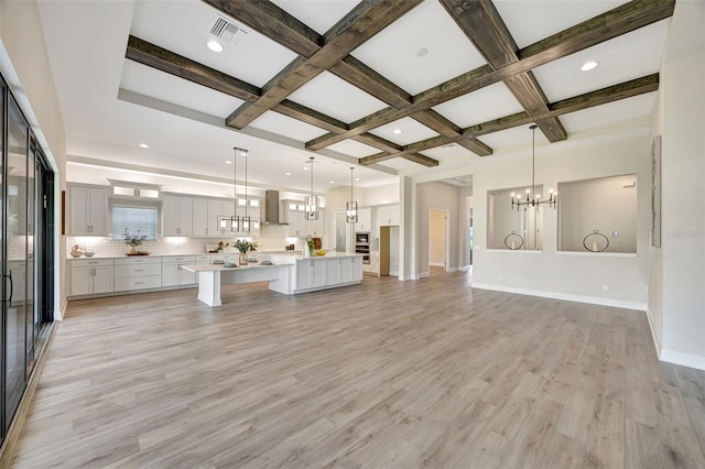 unfurnished living room with beam ceiling, an inviting chandelier, light wood-type flooring, and coffered ceiling