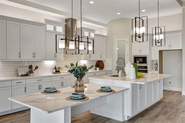 kitchen featuring sink, hanging light fixtures, an island with sink, built in microwave, and white cabinetry