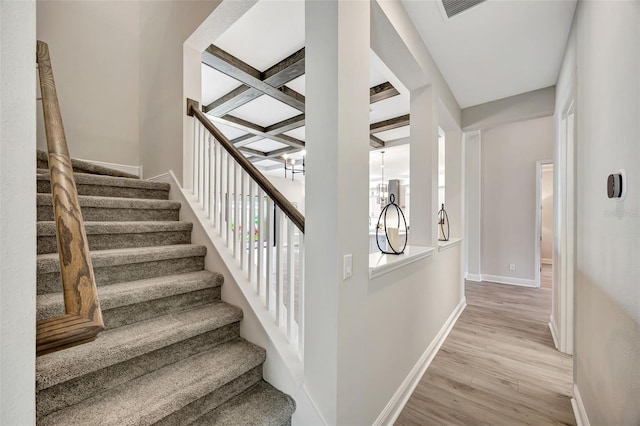 staircase featuring hardwood / wood-style flooring, a notable chandelier, beam ceiling, and coffered ceiling