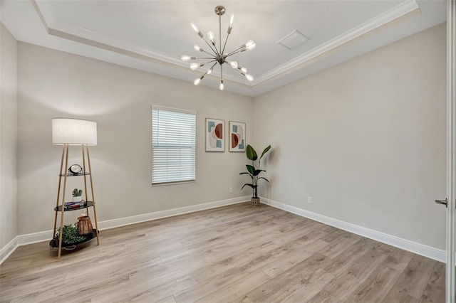 spare room with a raised ceiling, ornamental molding, light hardwood / wood-style floors, and an inviting chandelier