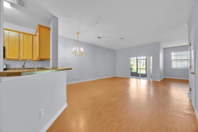 unfurnished living room featuring sink, light hardwood / wood-style flooring, and a notable chandelier