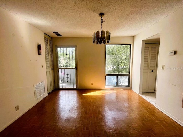 unfurnished dining area with dark parquet floors, a healthy amount of sunlight, a textured ceiling, and a chandelier