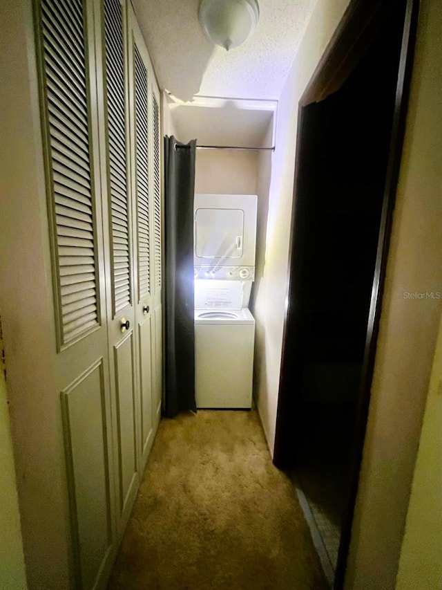 corridor featuring light carpet, a textured ceiling, and stacked washer and clothes dryer