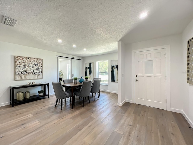 dining room with a barn door, a textured ceiling, and light hardwood / wood-style floors