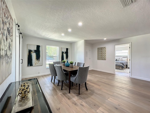 dining room featuring a textured ceiling, light wood-type flooring, and a barn door