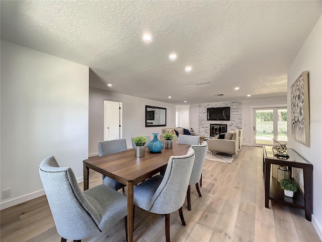 dining area featuring light hardwood / wood-style flooring, a brick fireplace, and a textured ceiling