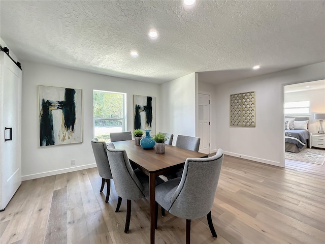 dining area featuring a textured ceiling, light wood-type flooring, and a barn door