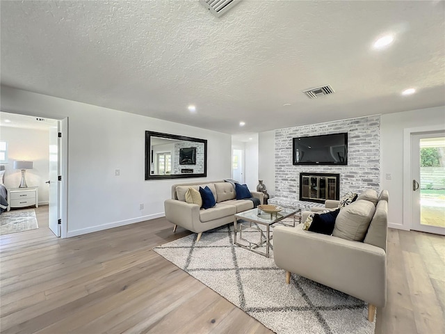 living room featuring a textured ceiling, light wood-type flooring, and a fireplace