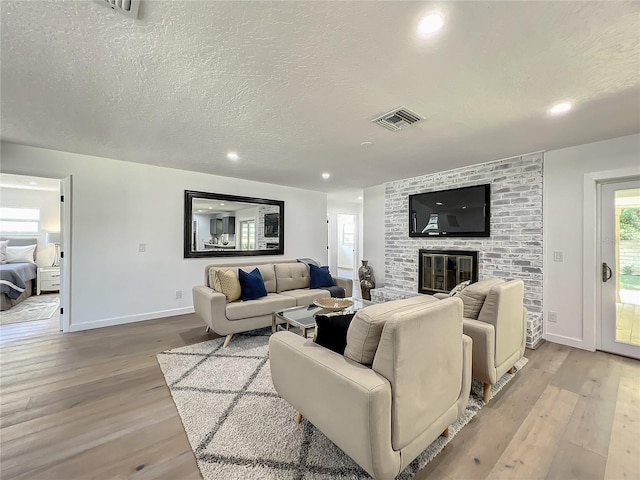 living room with light hardwood / wood-style flooring, a brick fireplace, and a textured ceiling