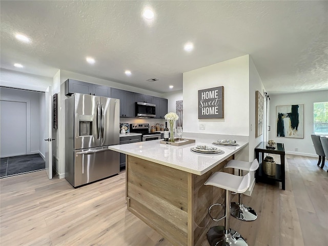 kitchen featuring light stone countertops, appliances with stainless steel finishes, kitchen peninsula, a kitchen breakfast bar, and light hardwood / wood-style floors