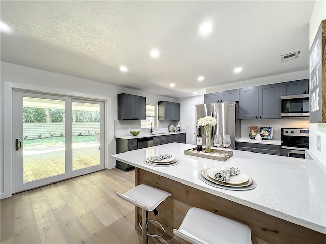 kitchen with light stone countertops, sink, light wood-type flooring, a kitchen bar, and stainless steel appliances