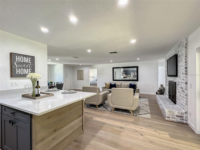 kitchen featuring a fireplace, light stone countertops, gray cabinets, a textured ceiling, and light hardwood / wood-style floors