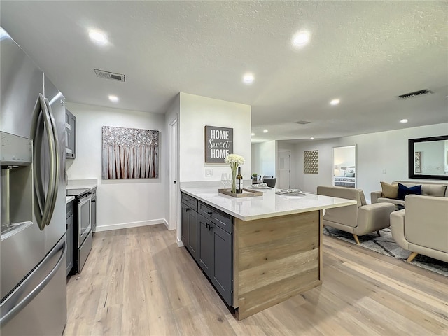 kitchen with light stone countertops, appliances with stainless steel finishes, light wood-type flooring, a kitchen island, and a textured ceiling