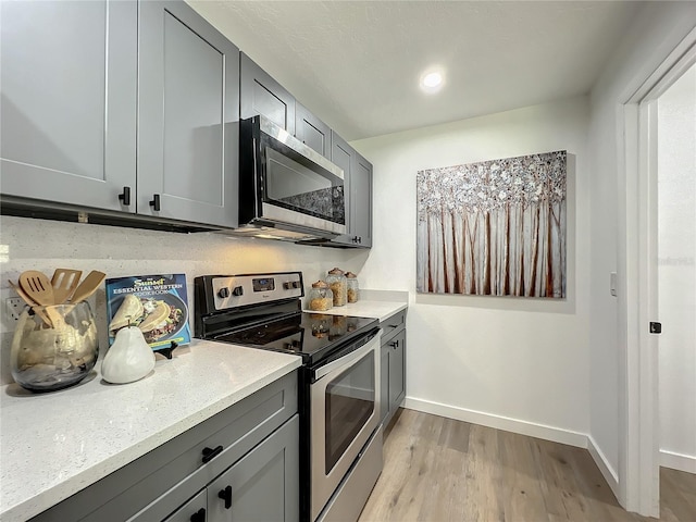 kitchen with light stone counters, stainless steel appliances, light wood-type flooring, and gray cabinetry