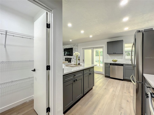 kitchen with light hardwood / wood-style floors, stainless steel appliances, a fireplace, and gray cabinetry