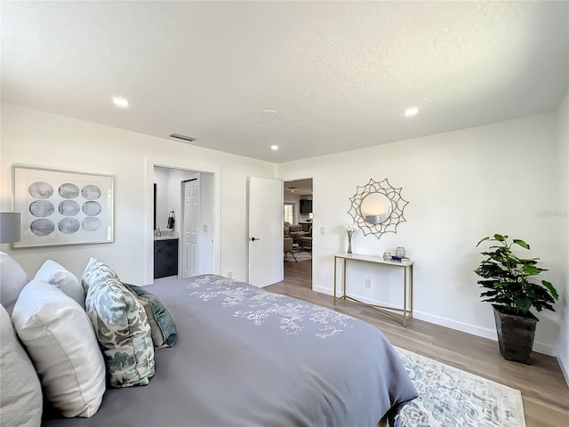 bedroom with ensuite bathroom, wood-type flooring, and a textured ceiling