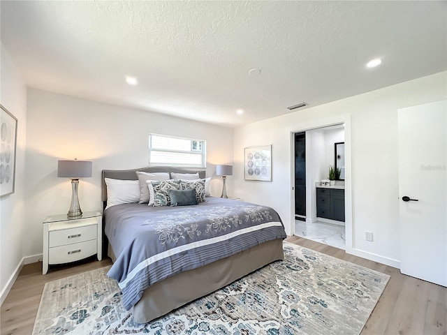 bedroom featuring ensuite bathroom, a textured ceiling, and light hardwood / wood-style flooring