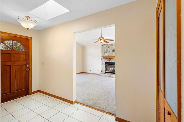 carpeted entryway with a stone fireplace, a skylight, and ceiling fan