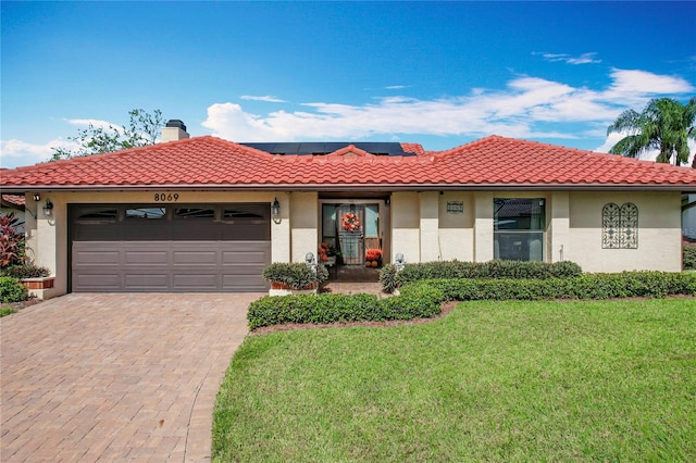 view of front facade featuring a garage, solar panels, and a front lawn