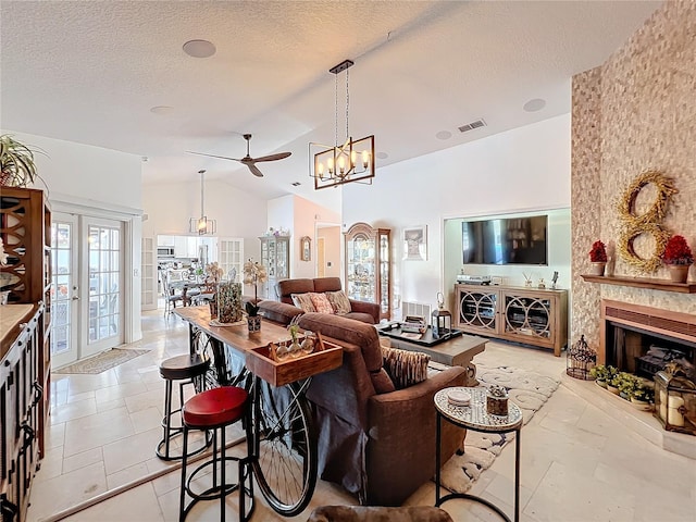 living room featuring french doors, ceiling fan with notable chandelier, vaulted ceiling, a textured ceiling, and a large fireplace