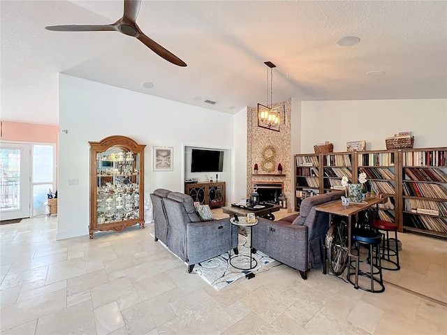 living room with ceiling fan with notable chandelier, a large fireplace, lofted ceiling, and a textured ceiling