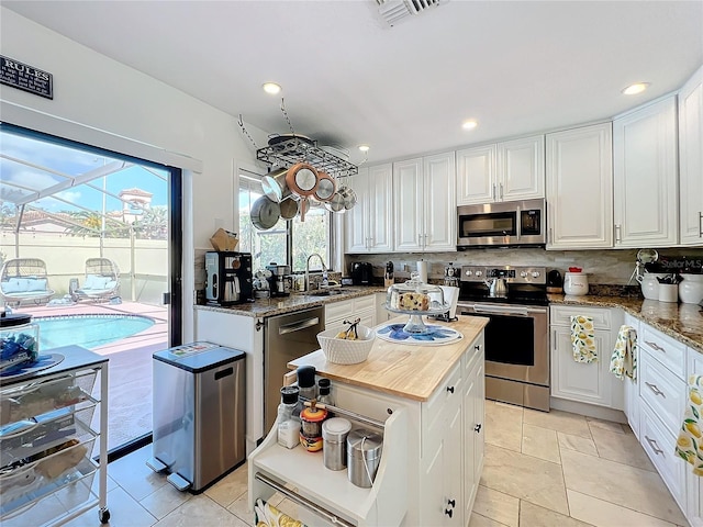 kitchen with light stone counters, appliances with stainless steel finishes, decorative backsplash, sink, and white cabinets