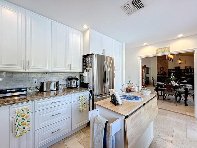 kitchen with stainless steel fridge, white cabinetry, decorative backsplash, and dark stone countertops