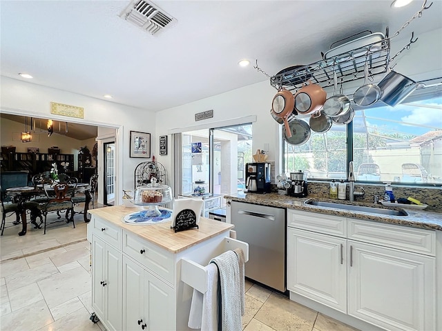 kitchen with stainless steel dishwasher, white cabinetry, sink, and dark stone counters