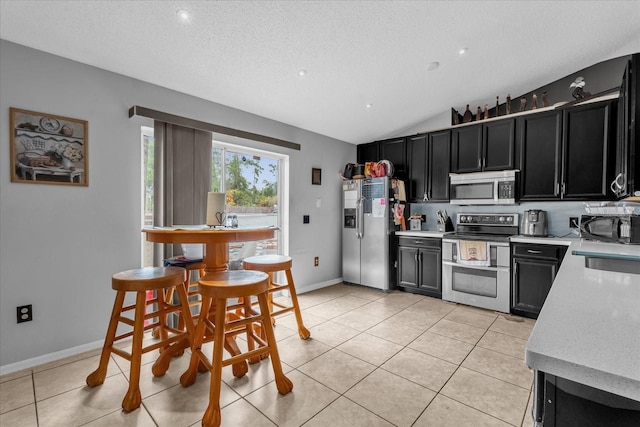 kitchen with light tile patterned flooring, lofted ceiling, stainless steel appliances, and a textured ceiling