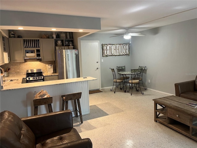 kitchen featuring a breakfast bar area, gray cabinetry, appliances with stainless steel finishes, kitchen peninsula, and backsplash