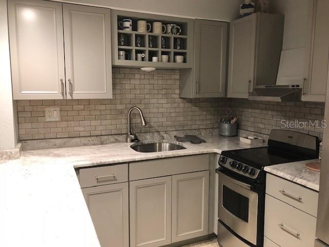 kitchen featuring stainless steel electric range oven, light stone countertops, sink, and decorative backsplash