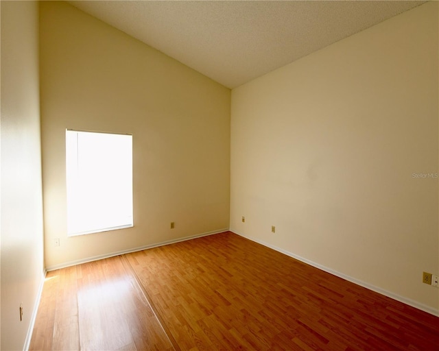 unfurnished room featuring hardwood / wood-style flooring, a textured ceiling, and vaulted ceiling