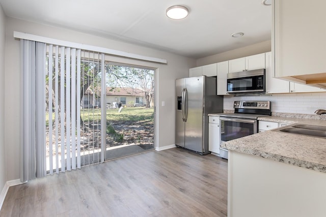 kitchen with light wood finished floors, stainless steel appliances, backsplash, white cabinets, and a sink