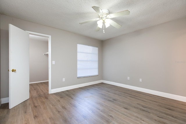 spare room with a textured ceiling, wood finished floors, a ceiling fan, and baseboards