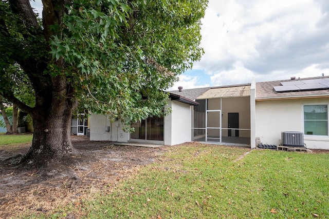 rear view of property featuring stucco siding, a lawn, central AC unit, a sunroom, and roof mounted solar panels