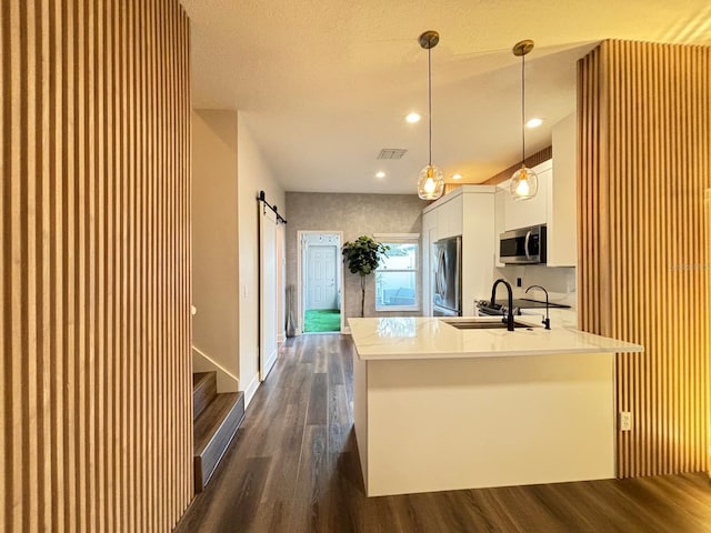 kitchen with white cabinets, dark hardwood / wood-style flooring, appliances with stainless steel finishes, a barn door, and pendant lighting