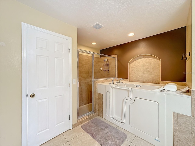 bathroom with a textured ceiling, independent shower and bath, and tile patterned floors