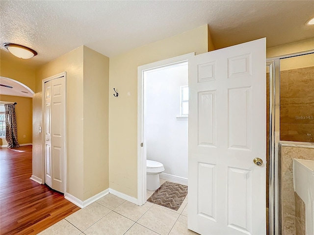 bathroom with tile patterned floors, a shower with shower door, a textured ceiling, and toilet