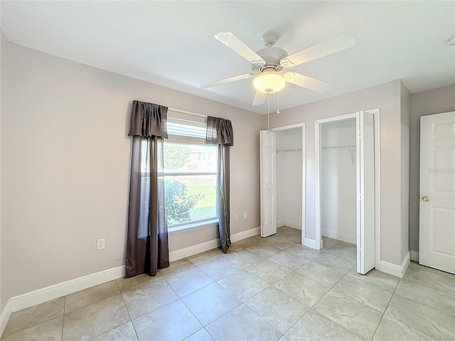 unfurnished bedroom featuring ceiling fan, light tile patterned floors, and two closets