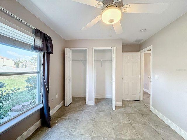 unfurnished bedroom featuring ceiling fan, multiple closets, and light tile patterned floors