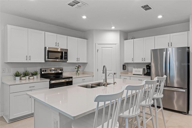 kitchen featuring white cabinets, an island with sink, appliances with stainless steel finishes, a kitchen breakfast bar, and sink