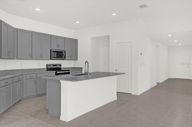 kitchen with stainless steel appliances, a sink, a center island with sink, and gray cabinetry