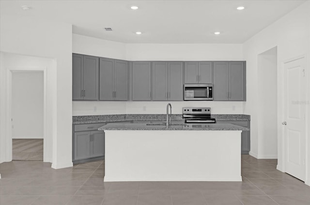 kitchen with a kitchen island with sink, gray cabinets, stainless steel appliances, stone counters, and a sink