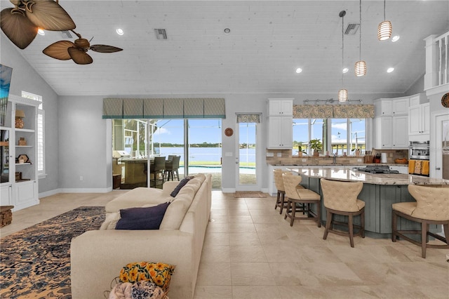 kitchen featuring light stone countertops, decorative light fixtures, white cabinets, a water view, and high vaulted ceiling