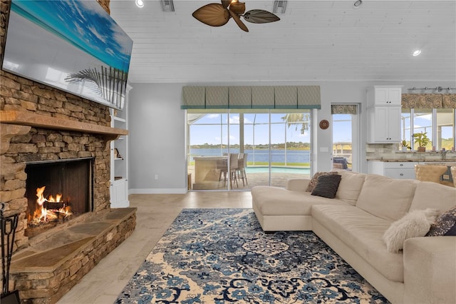 living room featuring a fireplace, ceiling fan, a water view, and a wealth of natural light