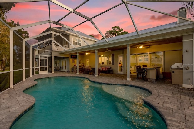 pool at dusk featuring a patio area, glass enclosure, and ceiling fan